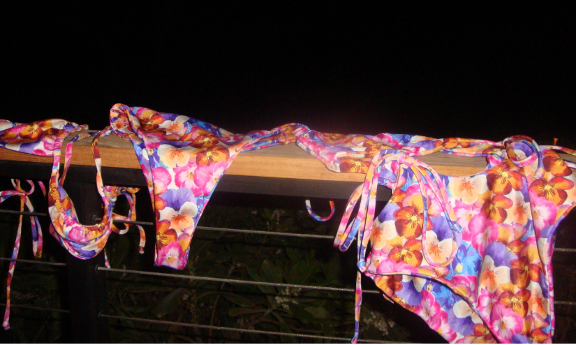 Colorful bikini set draped over a railing against a dark background